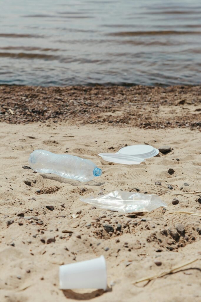 Plastic litter scattered on a sandy beach by the water's edge, highlighting pollution issues.